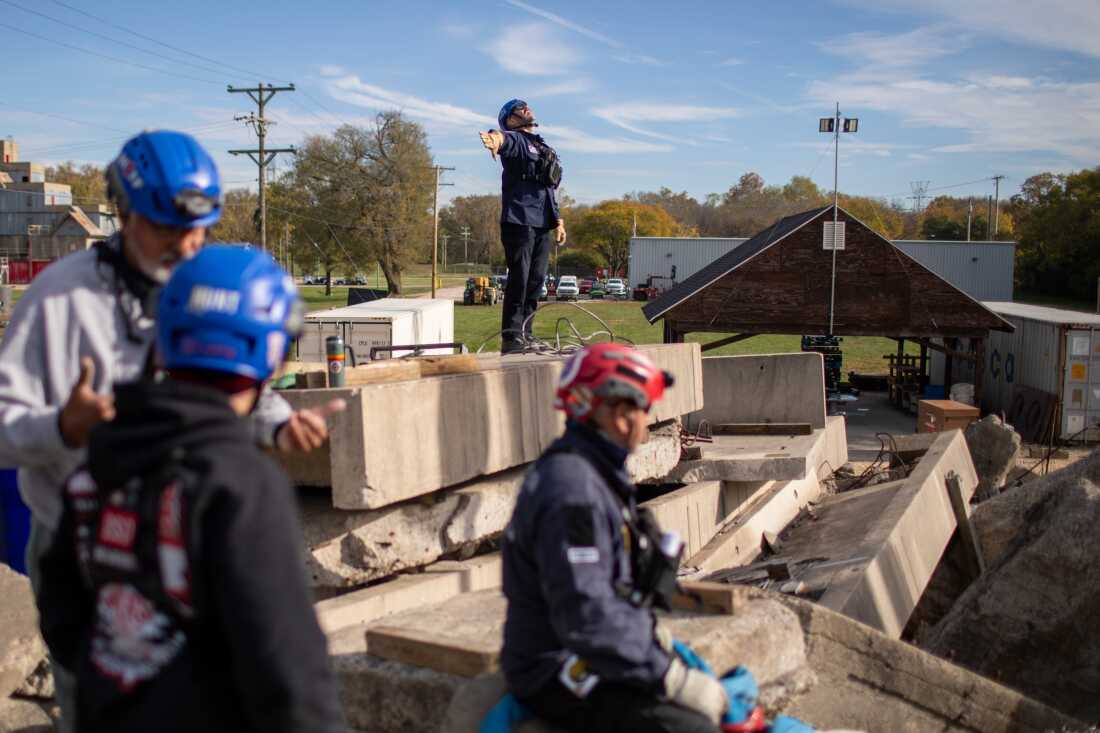 A search and rescue expert practices hand signals to communicate with a crane operator.
