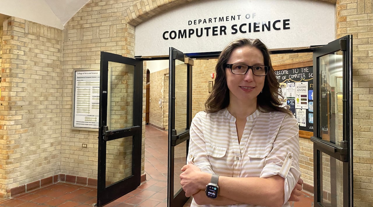 A woman stands in the hallway of a building with brick walls under a sign reading department of computer science.