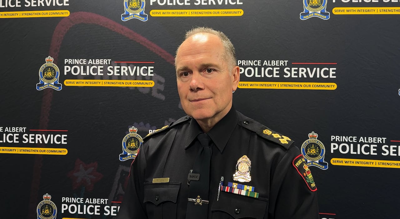 A man in a black police uniform stands in front of a backdrop printed with the police logo
