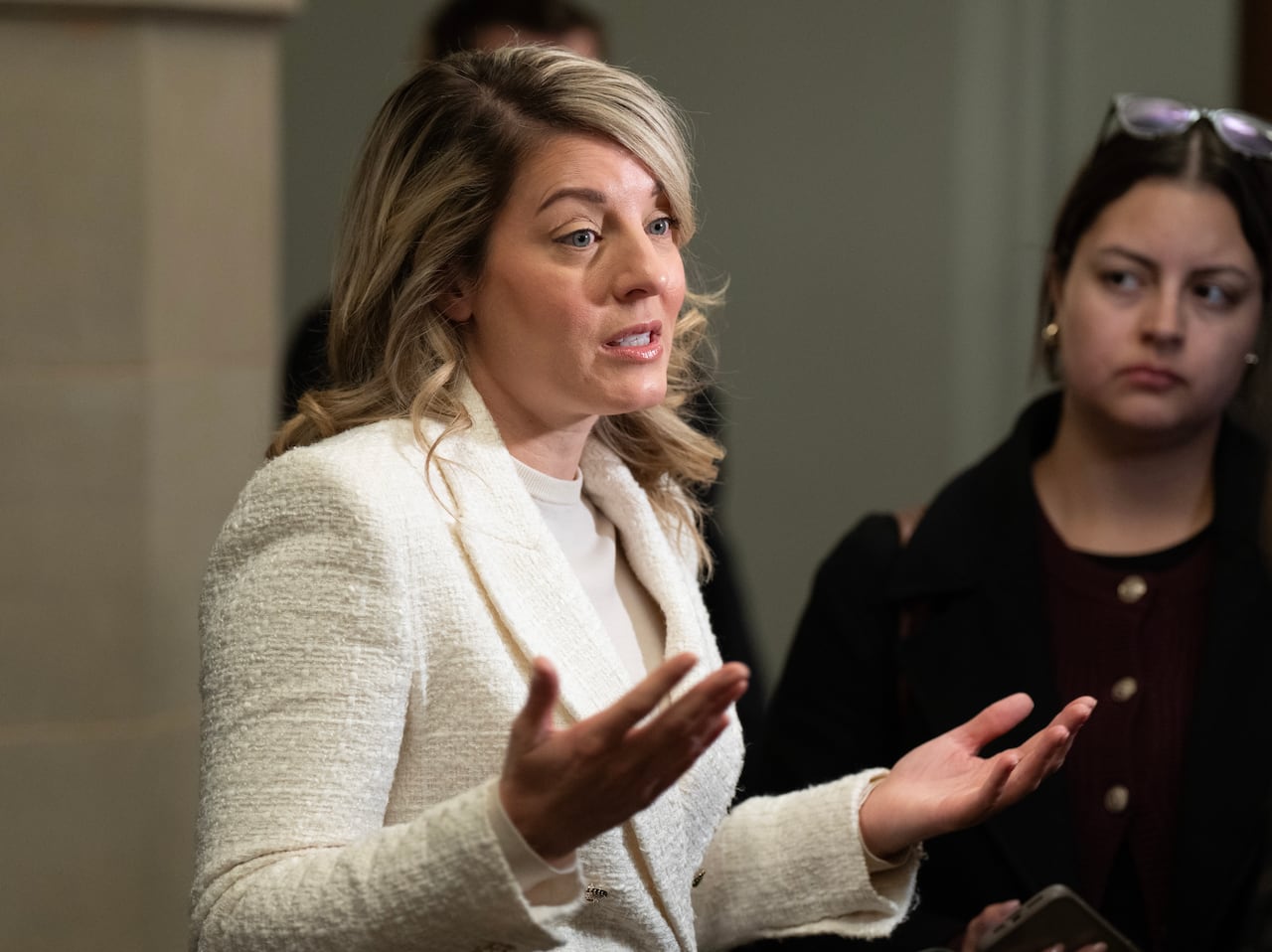 A woman wearing a white blazer speaks with reporters.