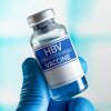 This photo shows a vial that's labeled "HBV (Hepatitis B Virus) Vaccine." A hand wearing a blue medical glove is holding the vial.