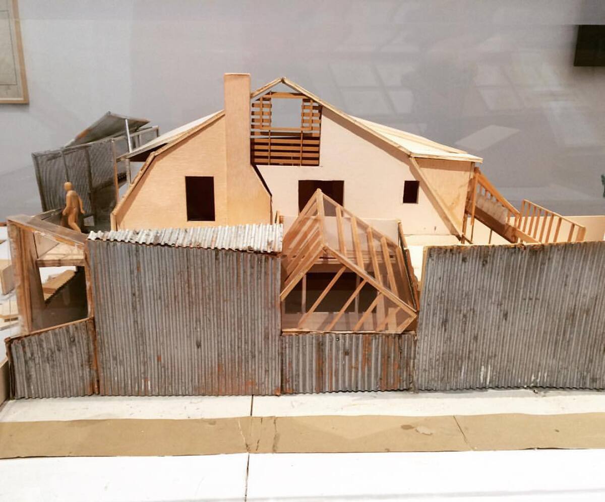 A wooden model shows corrugated metal surrounding a Dutch style house with a wooden cube protruding from a facade.