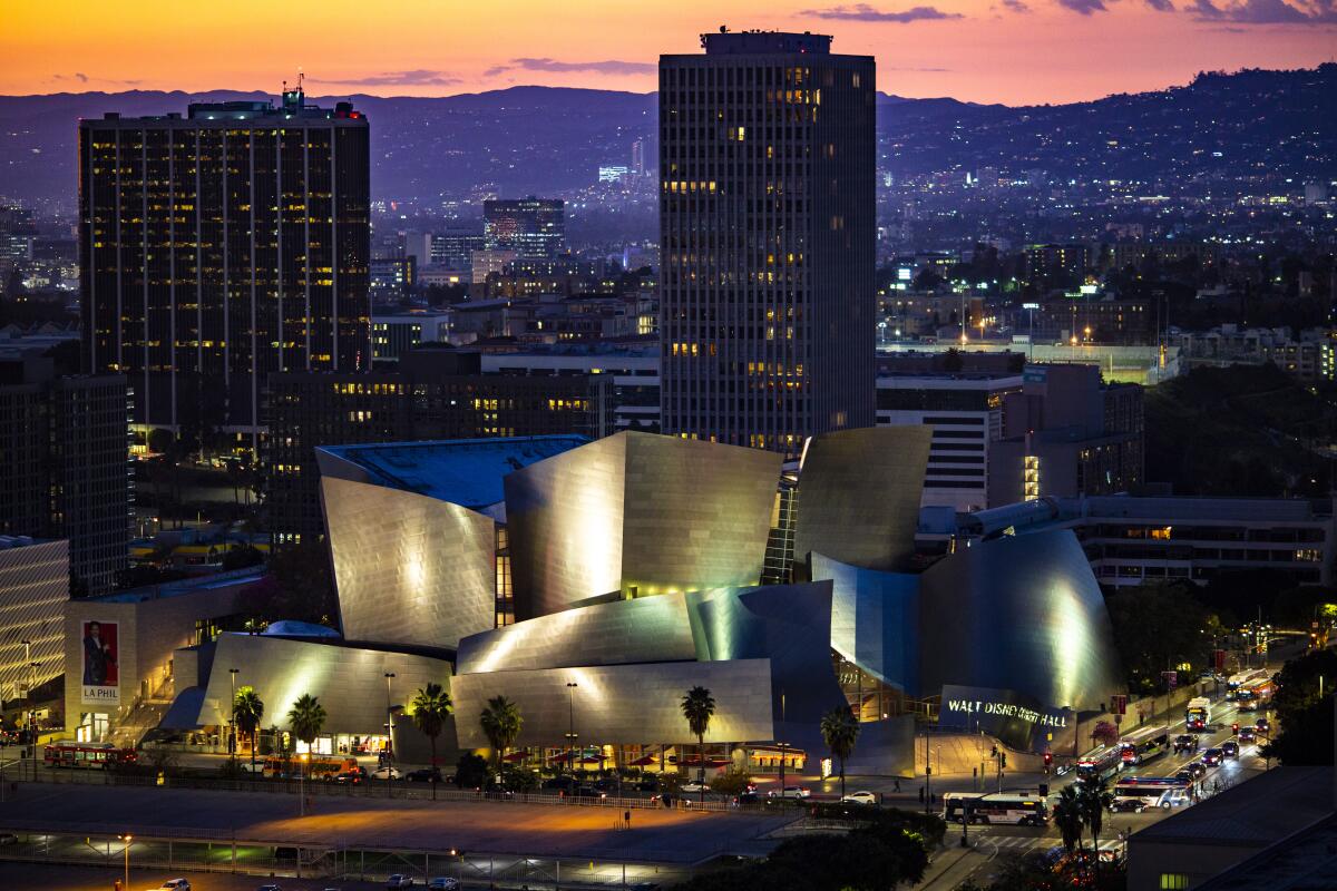 A view of Walt Disney Concert Hall at dusk as seen from above, with the hills and the lights of the city behind it.