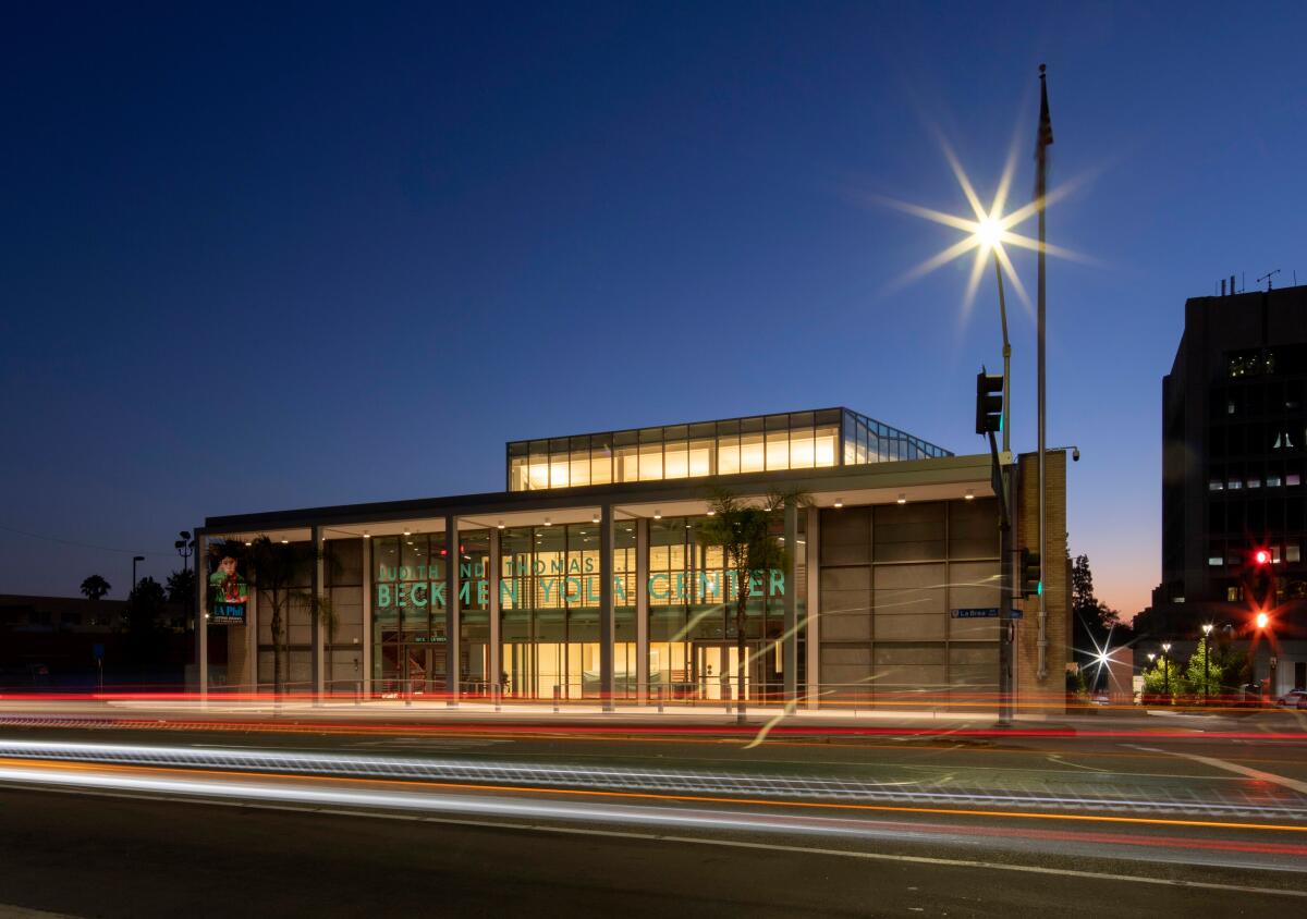 A horizontal view of the Beckmen YOLA Center illuminated at night, with the streaked lights of cars passing before it.