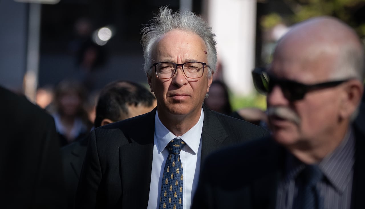 A man with white wavy hair is seen in a crowd outdoors.