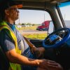 A.J. Jenkins, a truck operations specialist, observes an autonomous truck operating in no vehicle operator (NVO) mode during a route in Ellis County, Texas. He is in the driver's seat but his hands are in his lap while the truck is driving on a road. The steering wheel has a sign labeled "NVO Mode."