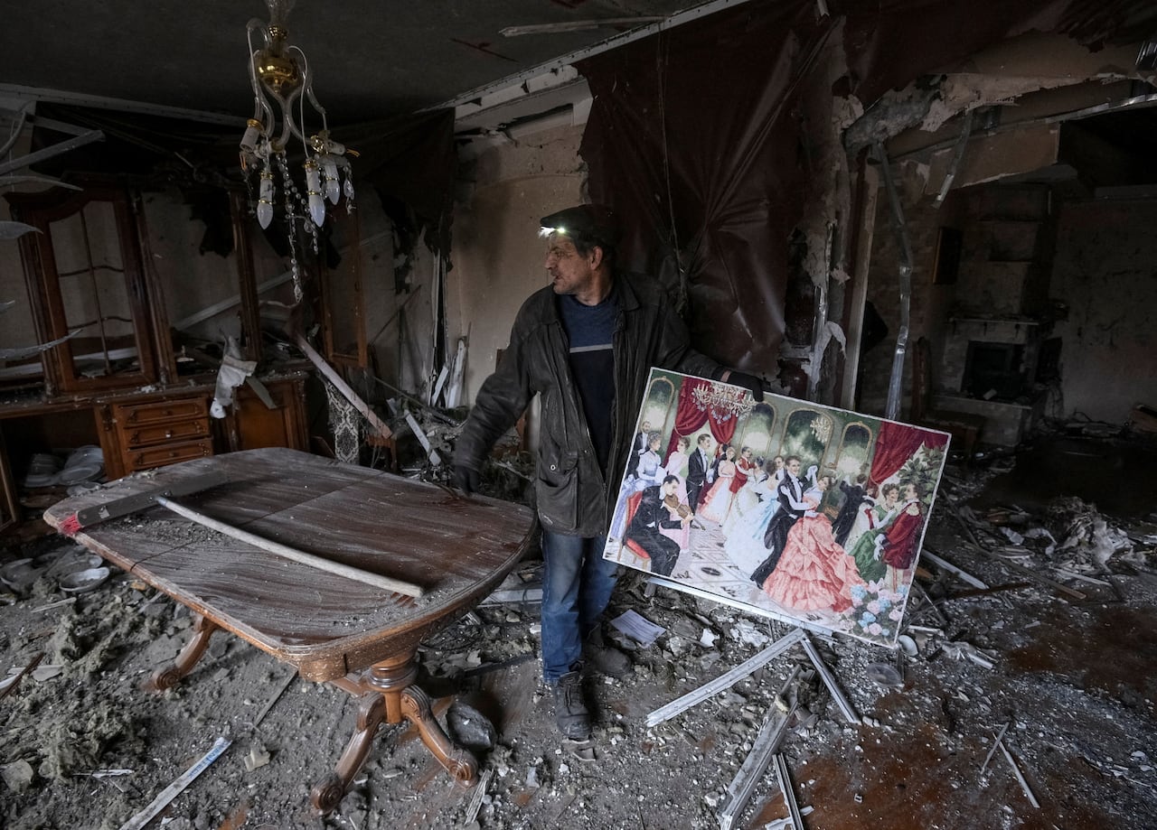 A man clutching a painting stands amid rubble and ruins