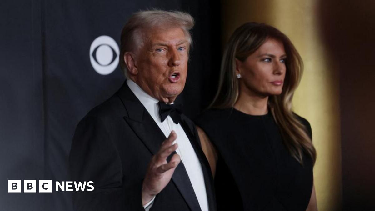 President Donald Trump and first lady Melania Trump pose on the red carpet for the 2025 Kennedy Center Honors. Trump, in a tuxedo, tooks towards the camera as he gesture while speaking to reporters