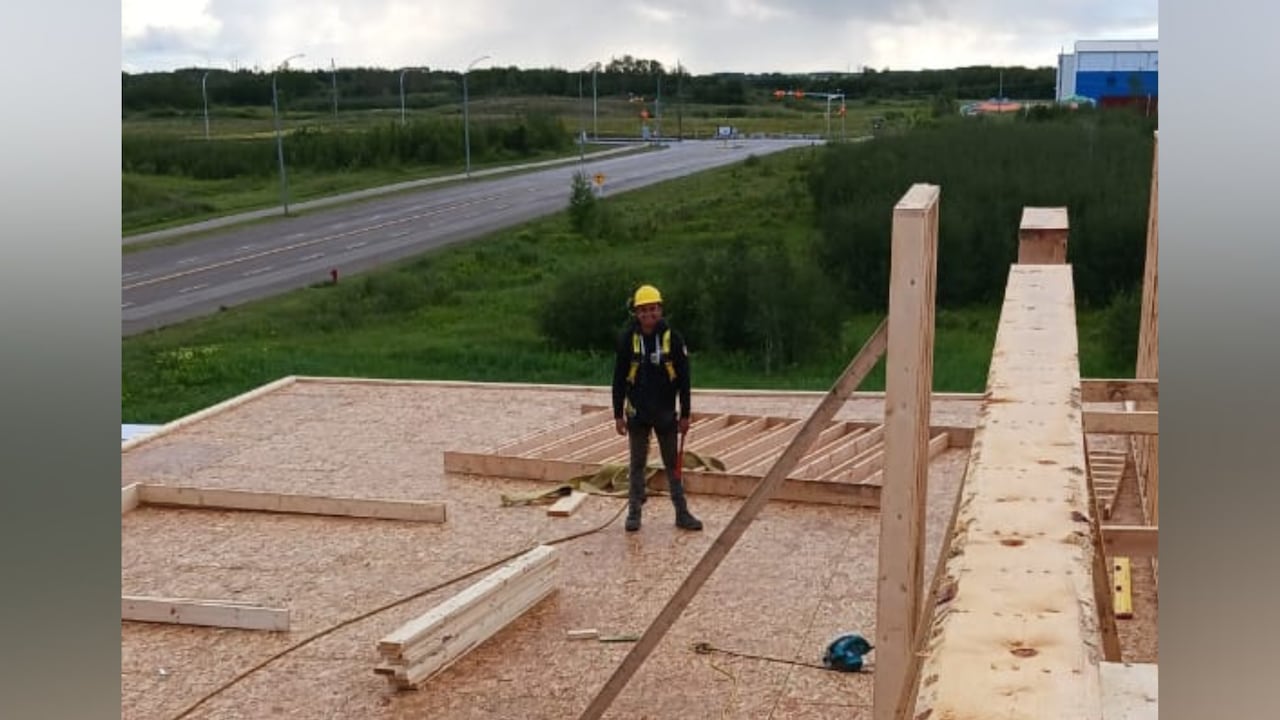 A man wearing a construction helmet standing on top of a structure under construction.