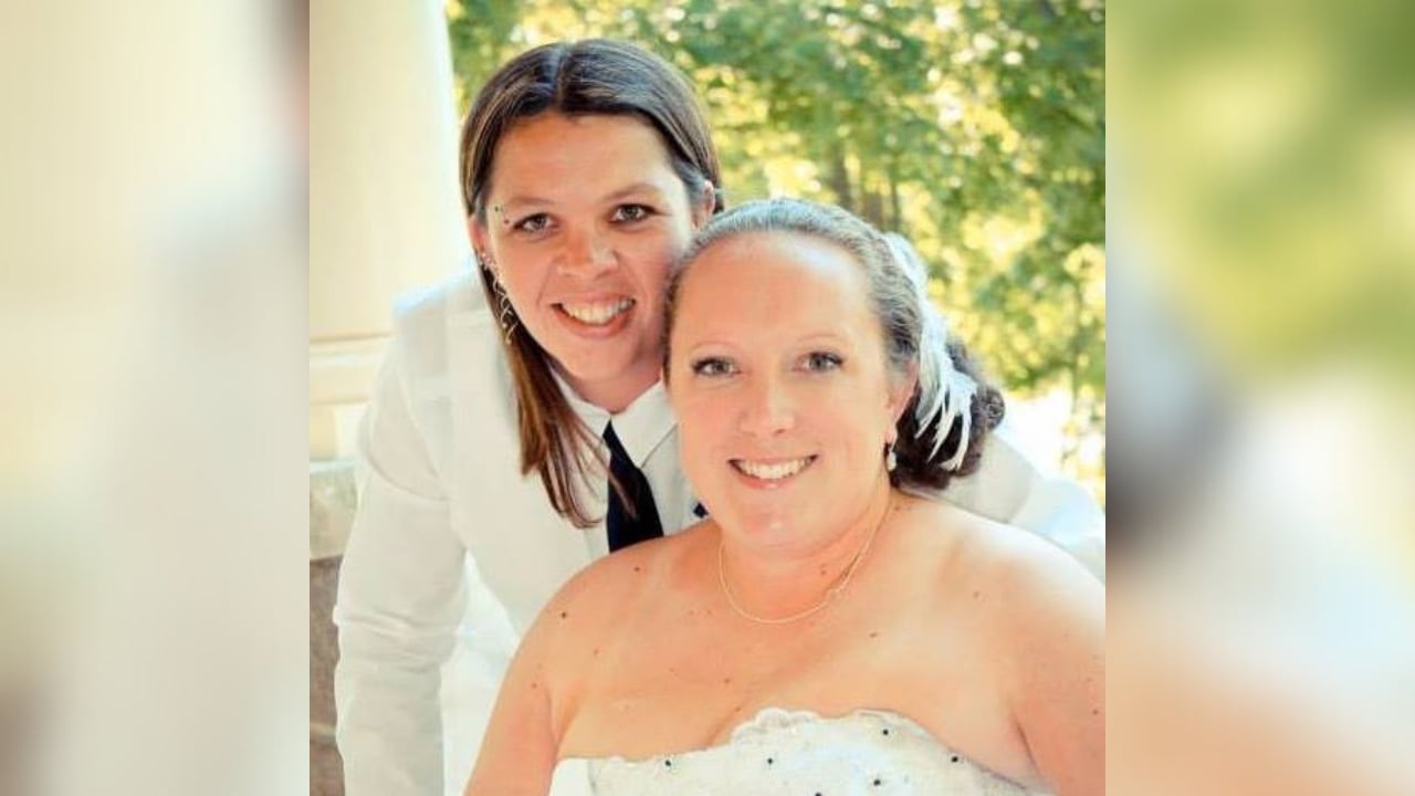 Two women in wedding attire smile. 