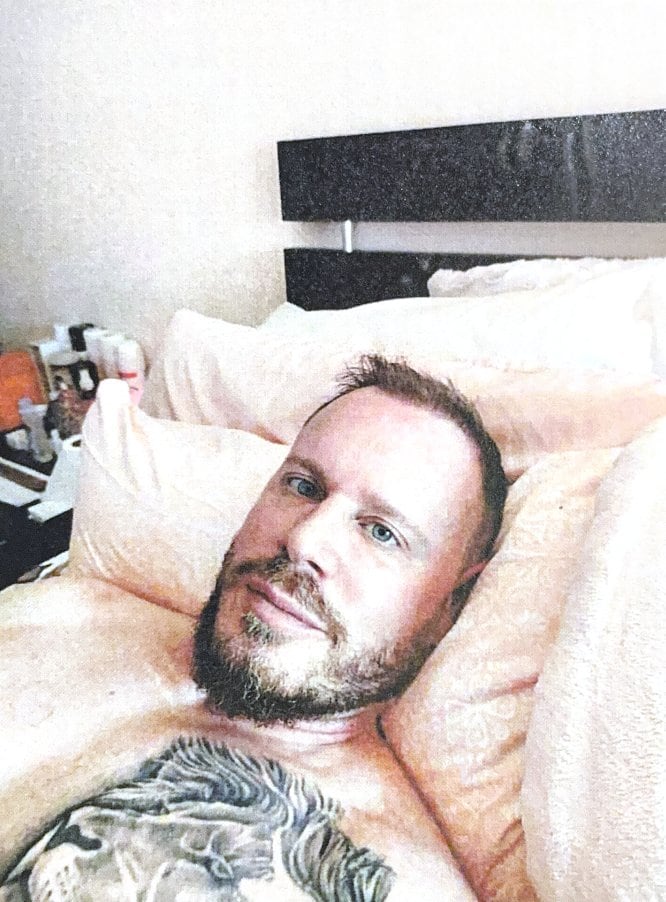 A man with a tattoo on his chest lies in a bed.