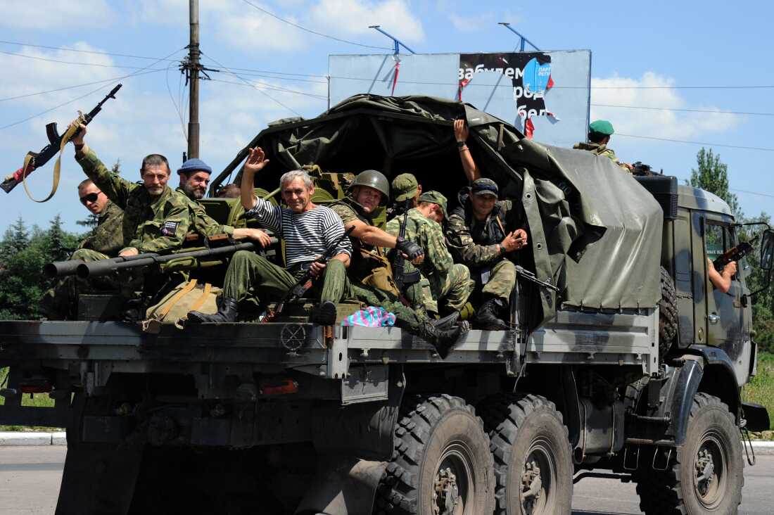 Pro-Russian militants sitting atop a truck drive past a checkpoint in Makiivka