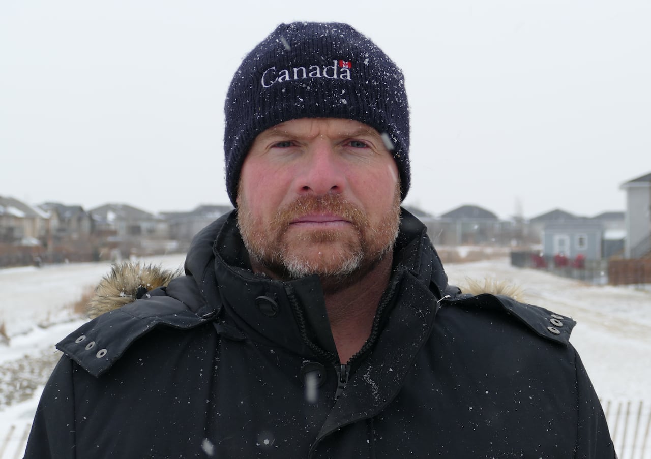A man in a toque that says "Canada" stands in snow.
