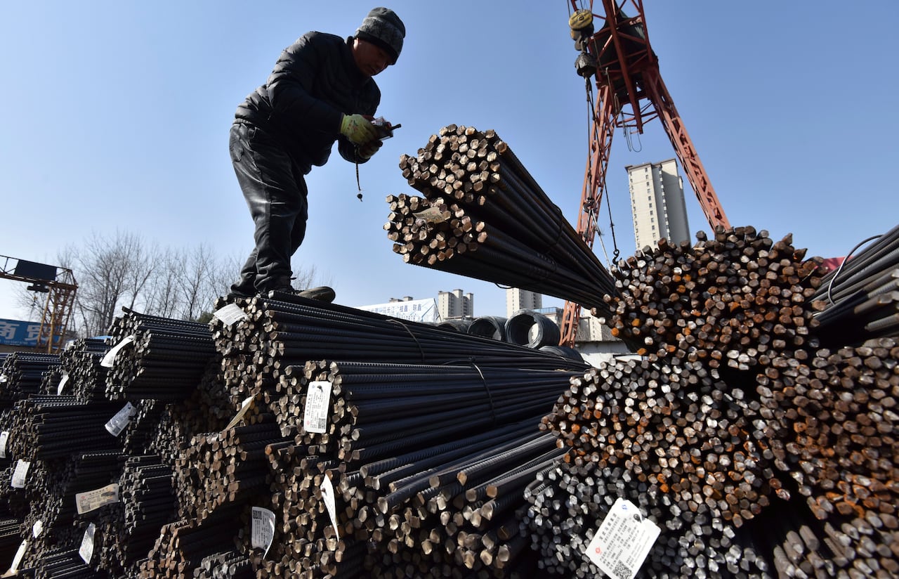 A worker, silhouetted against the sky, stands atop piles of rebar reinforced structural steel bars. 