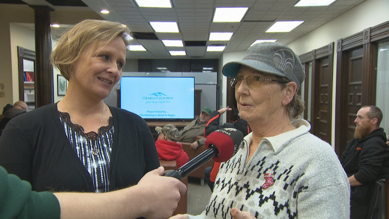 A blond woman with a sriped shirt and a cardigan stand with another woman wearing a gray pullover and hat standing in the lobby of Charlottetown City Hall.