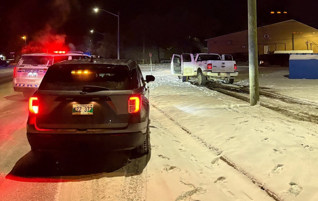 An RCMP cruiser is parked on a side of a snowy road while a white pickup truck is on the boulevard with its doors wide open.