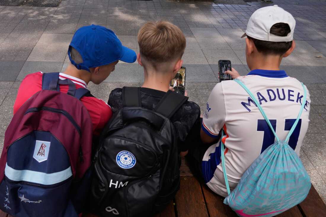 Hugo Winwood-Smith, right, Hardy Macpherson and Edan Abou, left, all 11-years-old, use their phones while sitting outside a school in Sydney on Monday, Dec. 8, 2025.