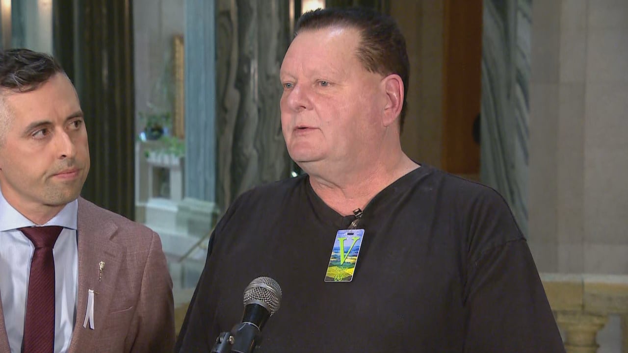 Two men stand next to each other while one speaks into a microphone