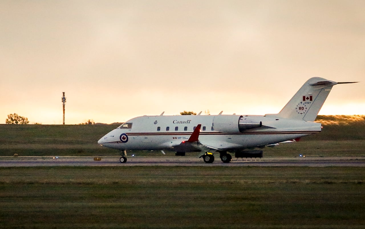 A white Challenger jet shown getting ready for take off on a runway at sunset.