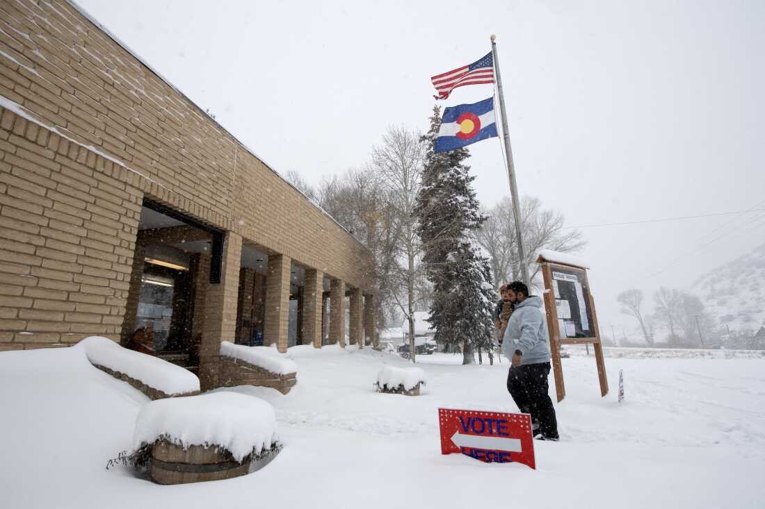 A voter carries his son as he walks into the Oak Creek Town Hall to drop off his ballot on Election Day, Nov. 5, 2024, in Oak Creek, Colo.