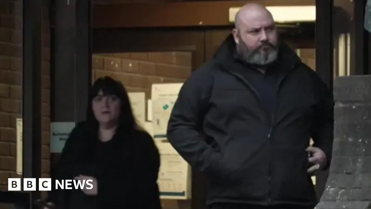 A picture of Hayley Bell, on the left, and Richard Elkin, on the right, coming out of Portsmouth Crown Court. Hayley Bell is wearing a black coat and has long, dark hair. Richard Elkin is bald and has a white and grey beard.
