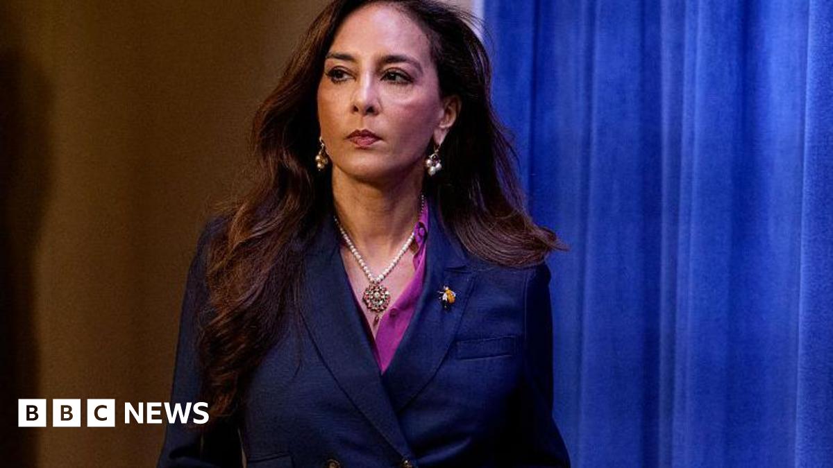 Assistant Attorney General Harmeet Dhillon, of the Justice Department's Civil Rights Division, walks into a press conference. A blue velvet curtain serves as a backdrop.