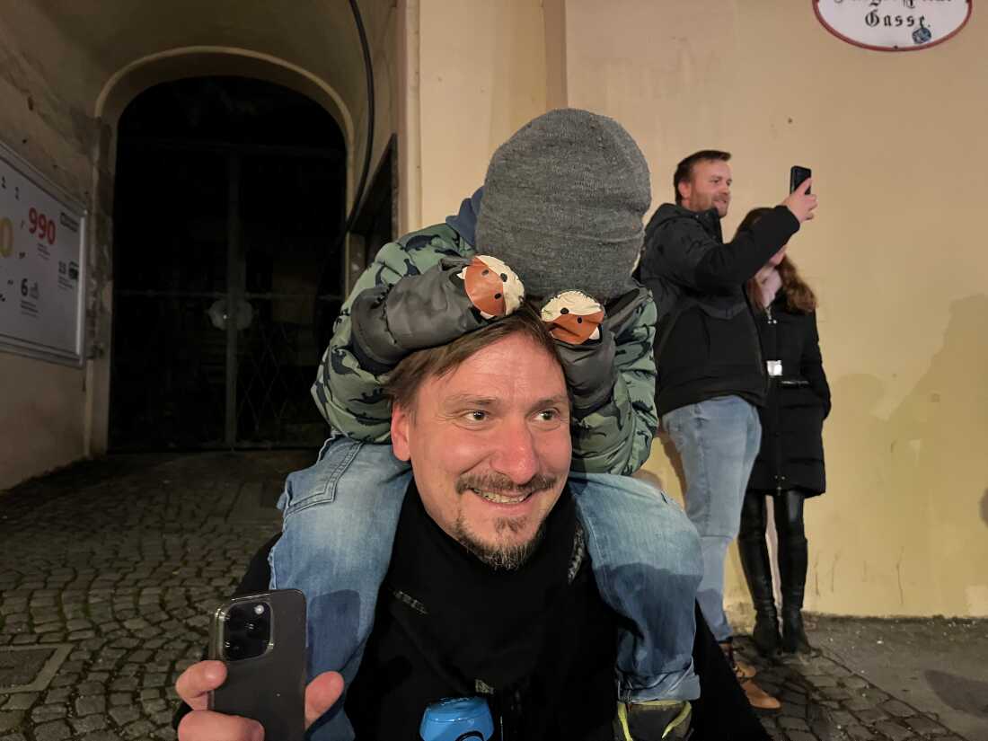 Salzburg resident Rene Watziker watches the Krampuses go by, but his four-and-a-half year-old son Valentin perched is too scared to look at them.