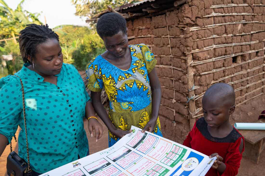 Kyatiremu Justine (center), 50, and her coach from the AVSI Foundation coach (left) look over records showing the progress in her business of buying and selling pigs.