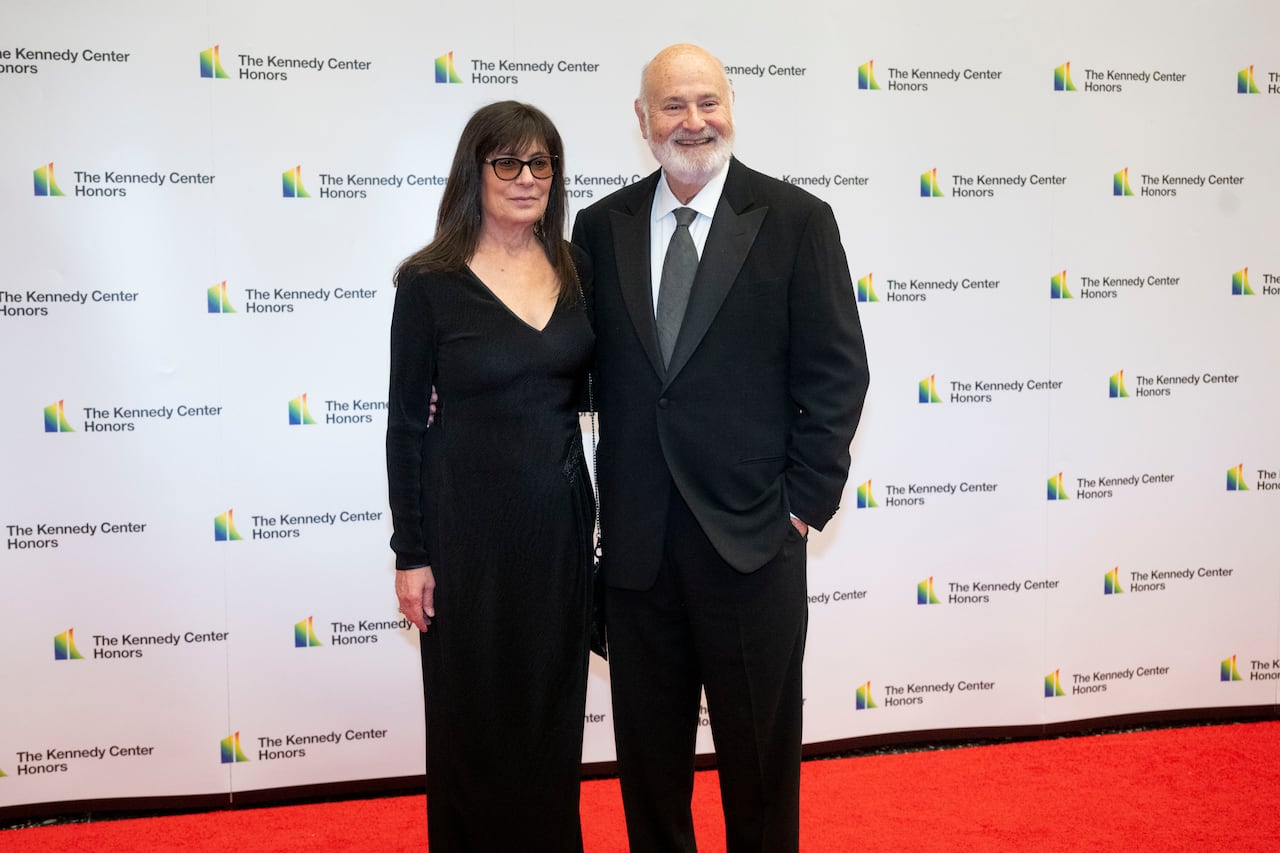 A woman in a black dress and a man in a suit pose for a photo on a red carpet in front of a backdrop that says The Kennedy Center Honors.