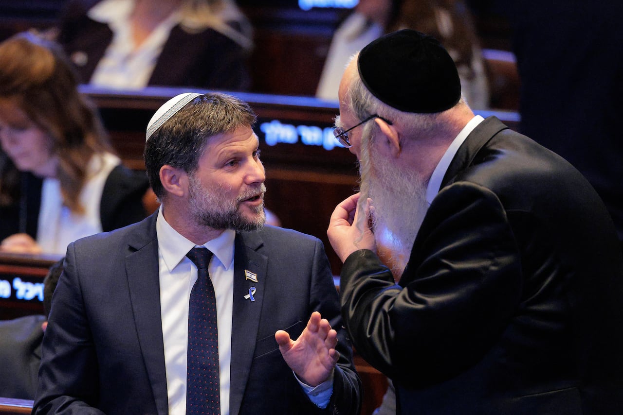 Two men in suits and yarmulke speak to each other.