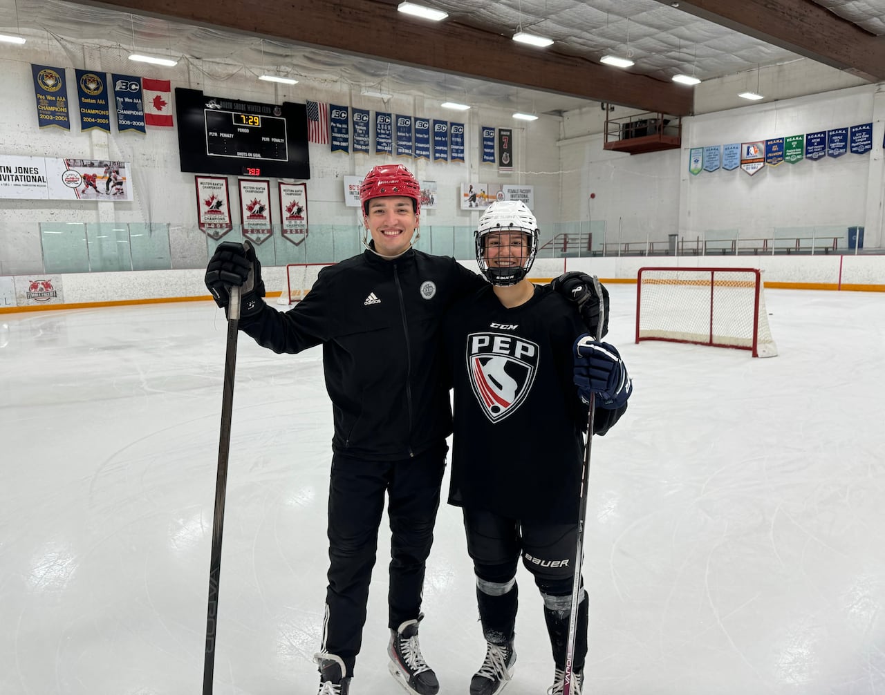 A man and a female hockey player pose for a photo on a hockey rink.