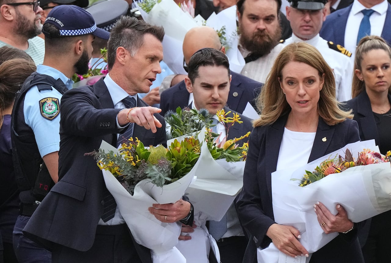 A man and a woman each hold bouquets of flowers while wearing dark clothing. 