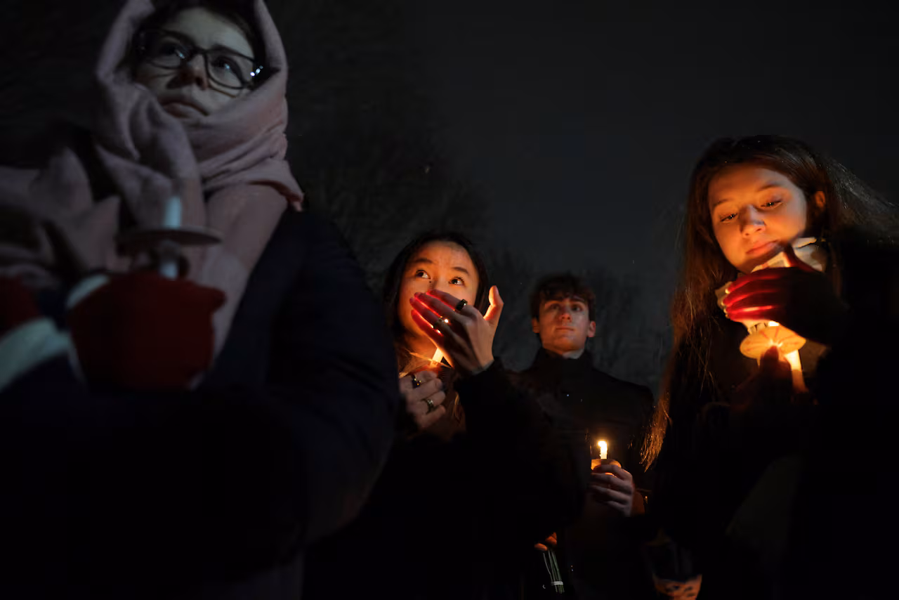 Four young people are shown holding candles at a night vigil.