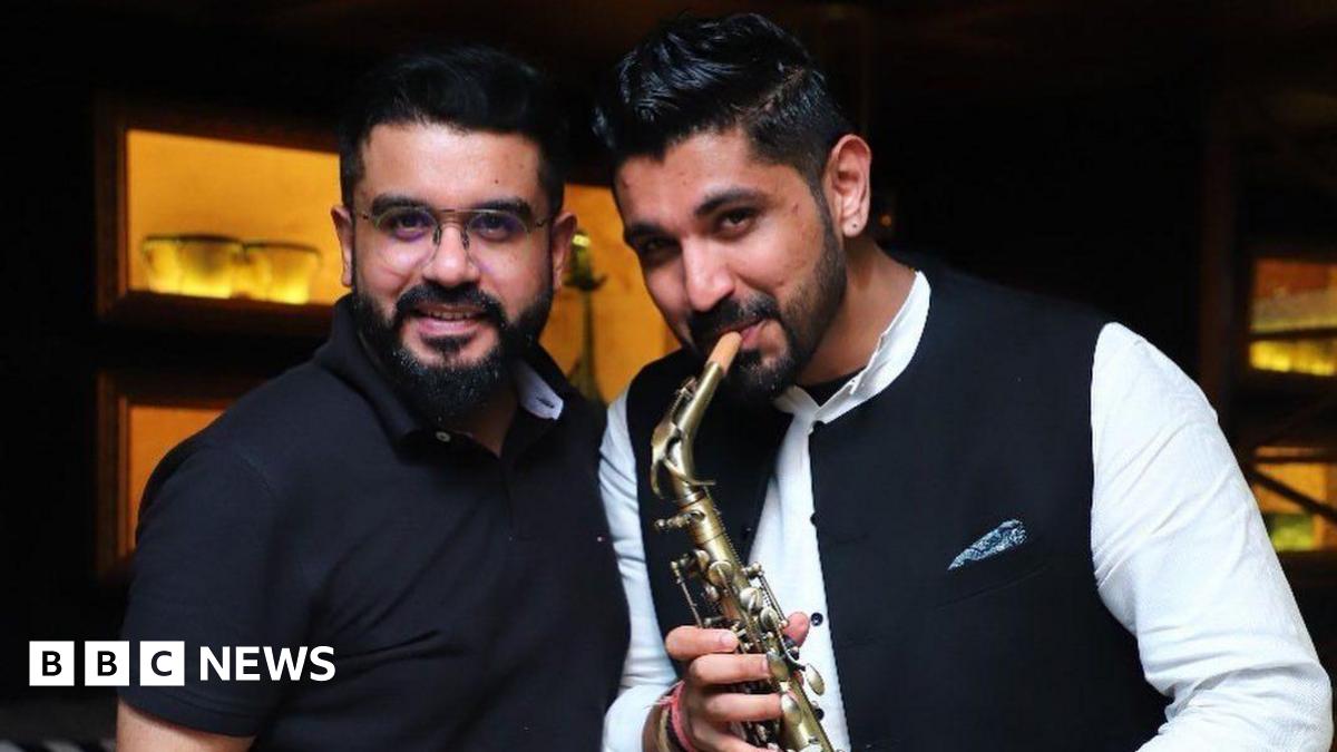 Saurabh Luthra (R), wearing a white shirt and holding the saxophone, stands with his brother Gaurav Luthra (L), who is wearing a black half sleeved shirt, for a picture.
