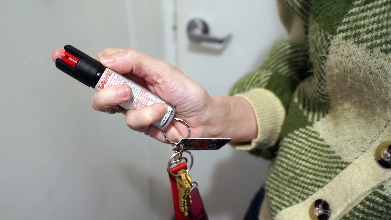 A woman holds a small cylinder with a warning label and bright red cap is shown hanging from a lanyard with keys.