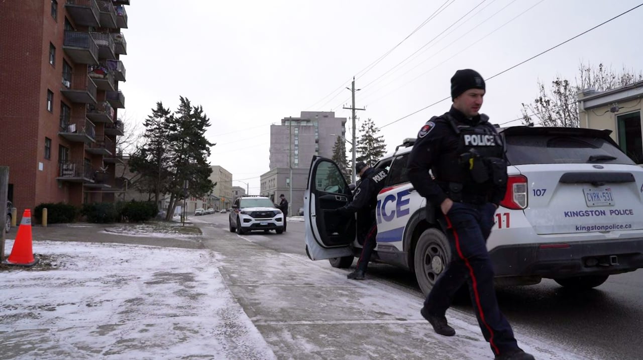 Three police officers can be seen walking to their cruisers outside a tall, orange-brick building.