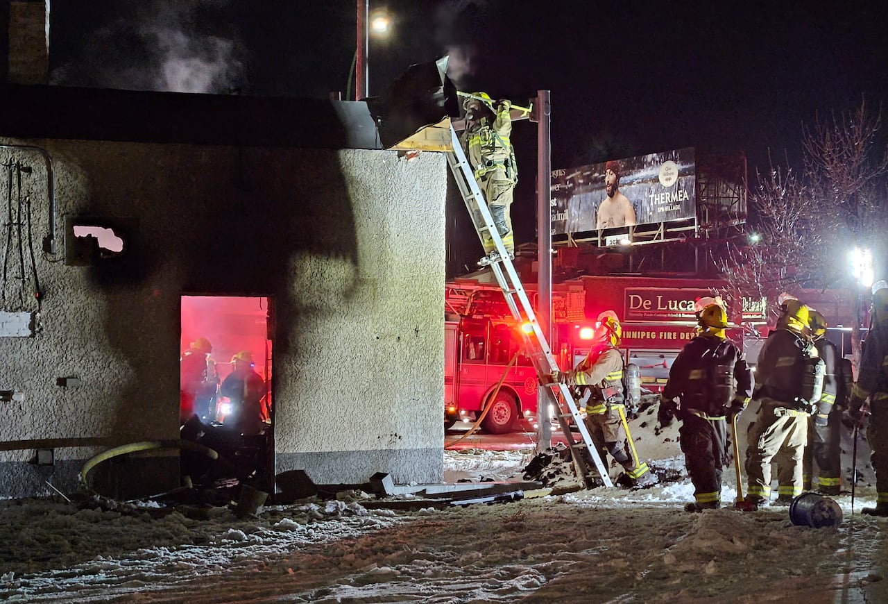 Firefighters climb a ladder to the top of a one-storey building while others are seen inside through an open door.
