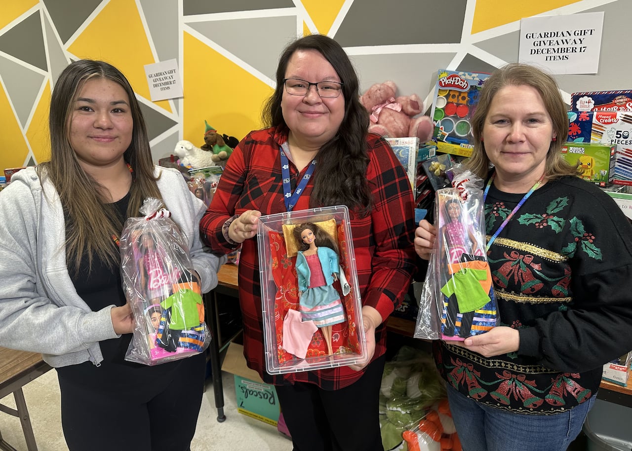 Three women pose with Barbie dolls and hand-made ribbon skirts