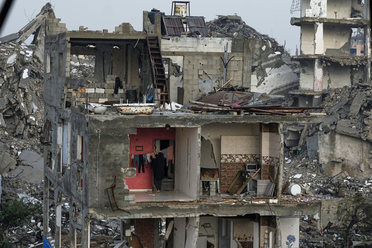 A woman hangs laundry in a building that has exposed walls and is partially destroyed.