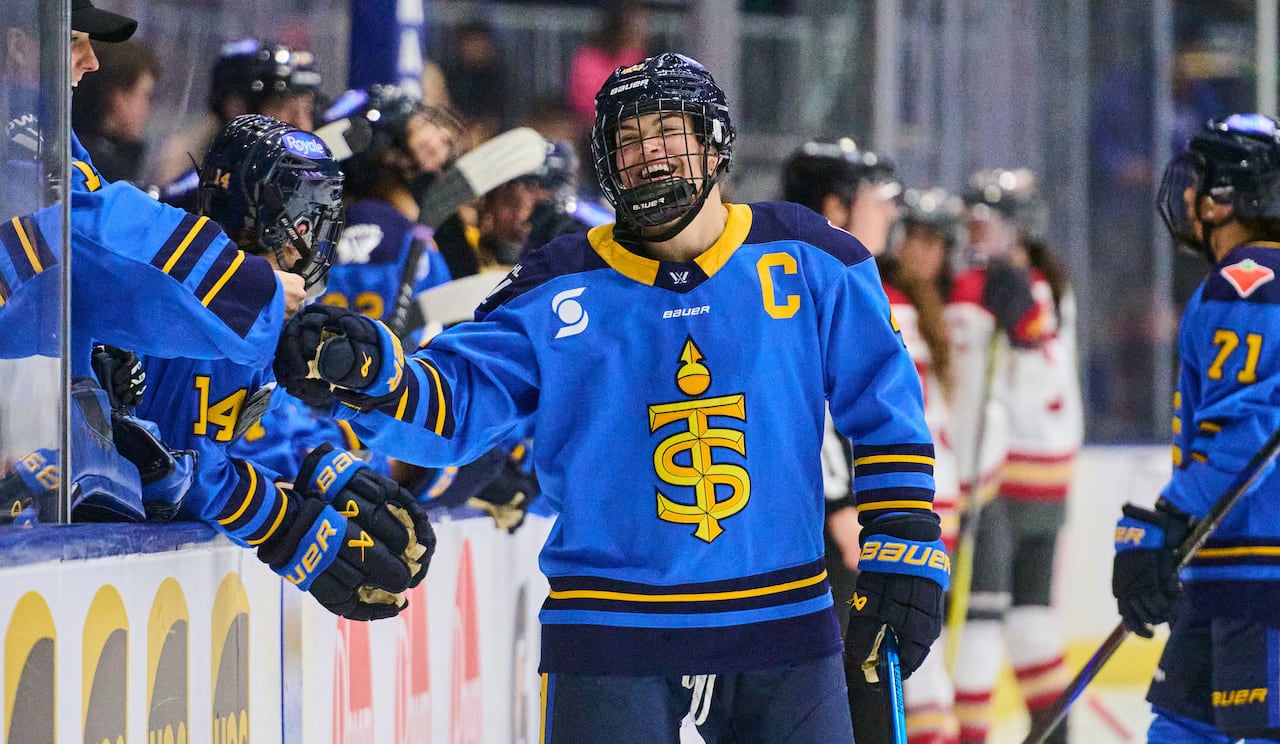 A hockey player celebrates with her teammates on the bench.