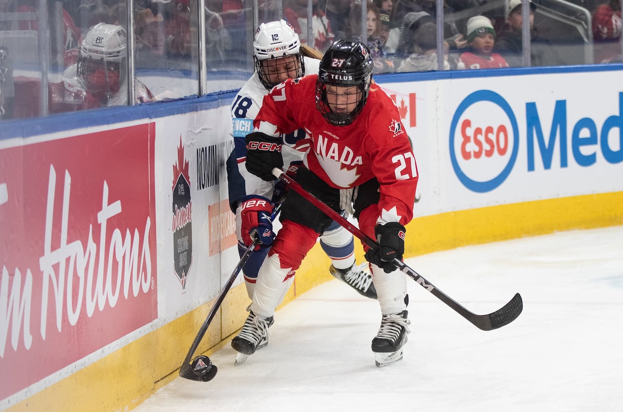 Two hockey players battle for the puck along the boards.