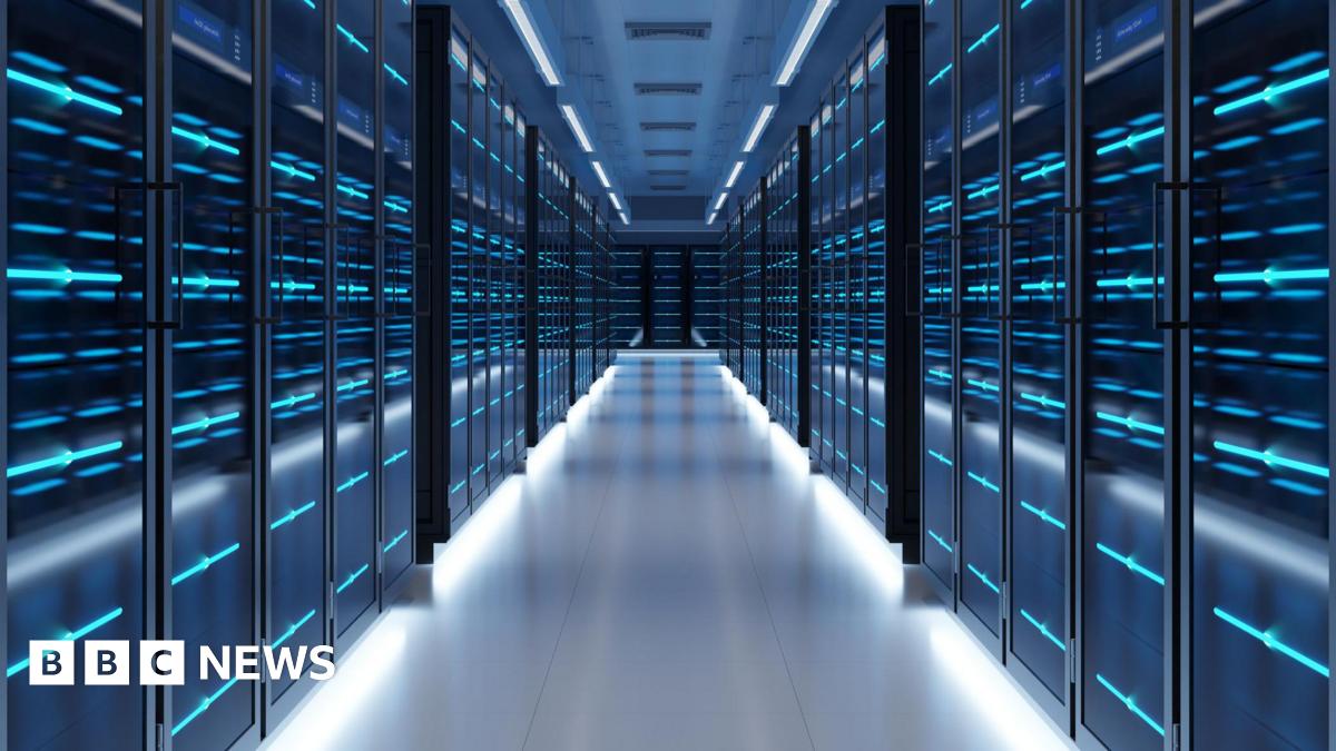 A view of a data centre corridor lined with dark cabinets covered in lights. The mood is sinister.