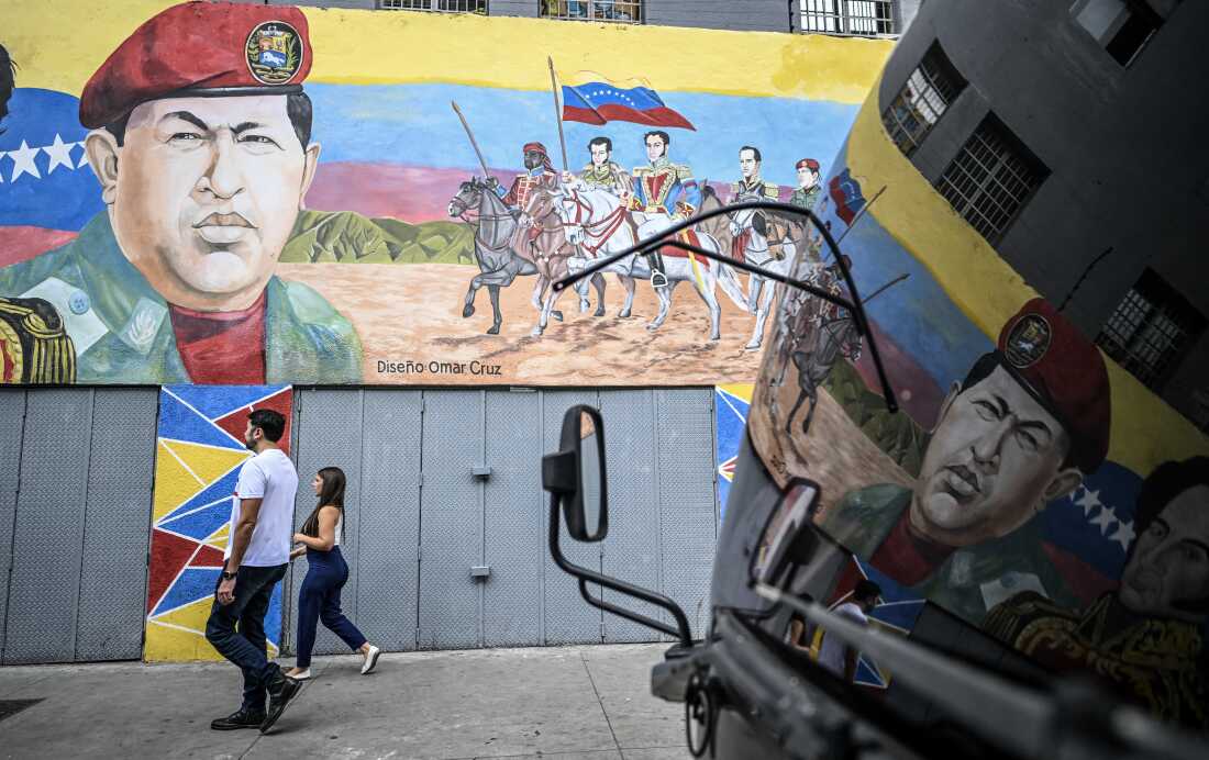 People walk past a mural depicting former Venezuelan president Hugo Chavez alongside Venezuelan independence heroes in Caracas on Dec.17, 2025. 