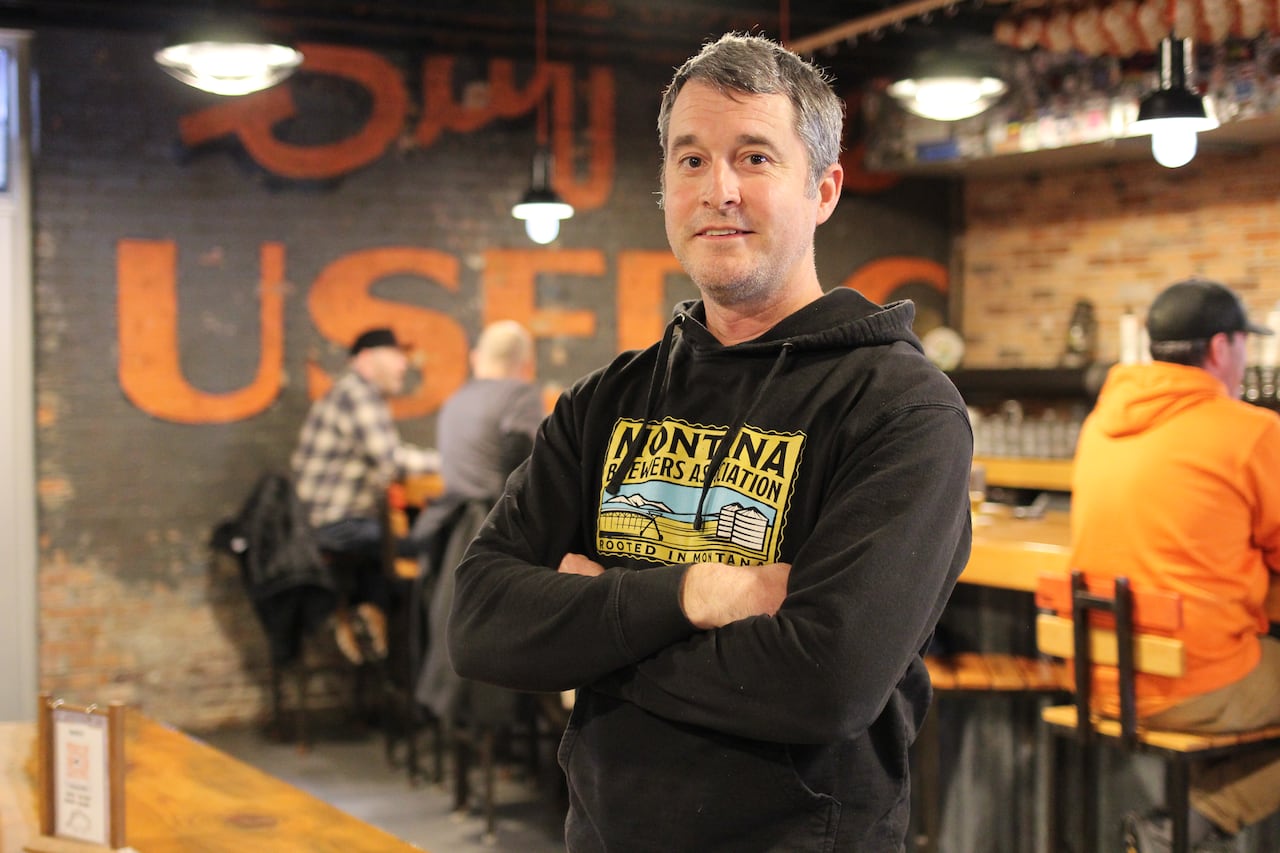 A man in a black hoodie poses with his arms crossed at a brewery.