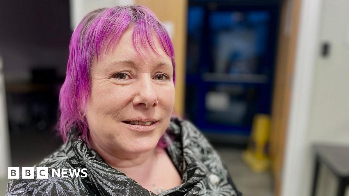 Leanne Nagel poses close to the camera. She has dyed purple hair and is wearing a black patterned blouse.
