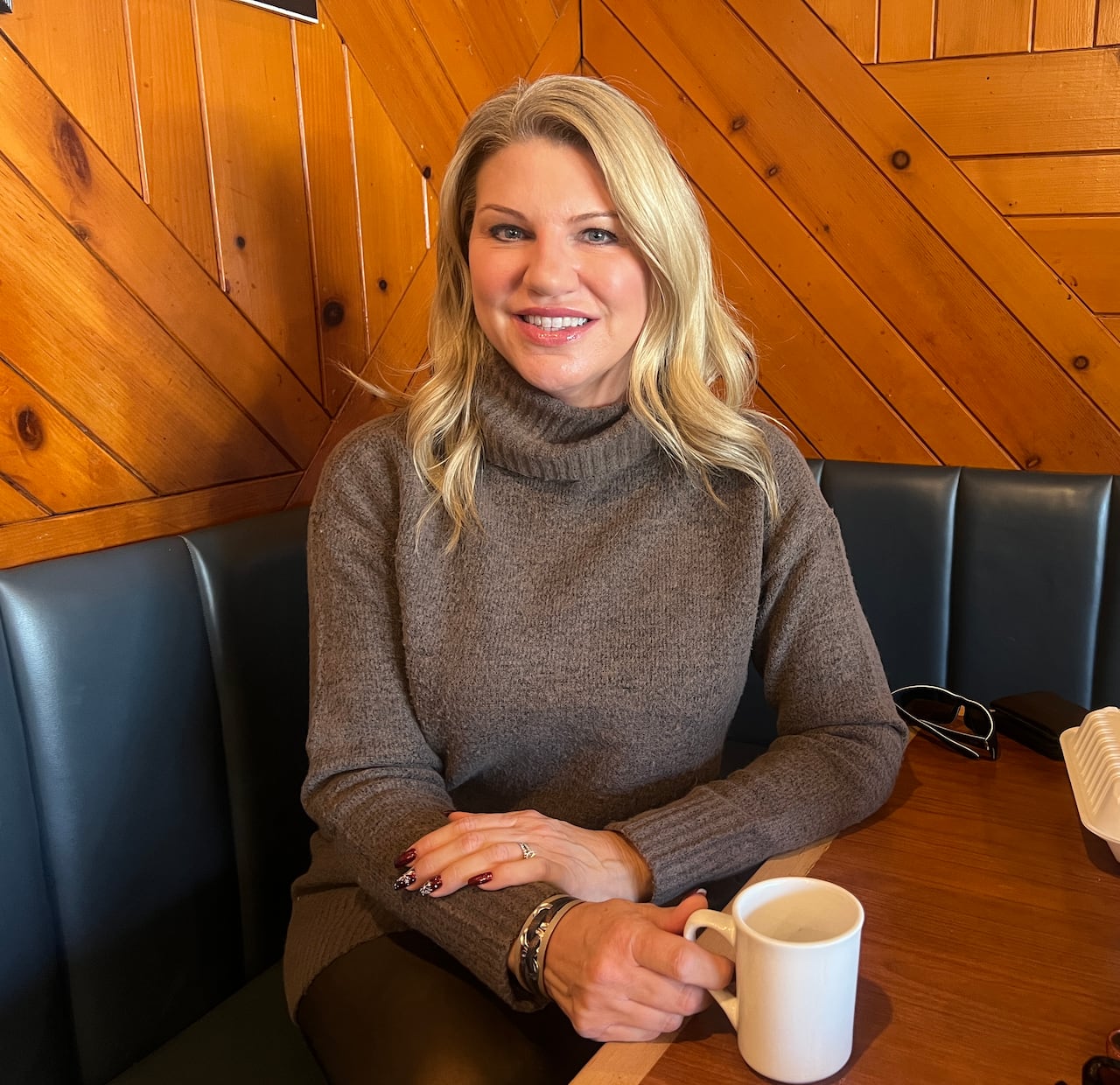 A picture of a woman in a restaurant with a coffee cup smiling.