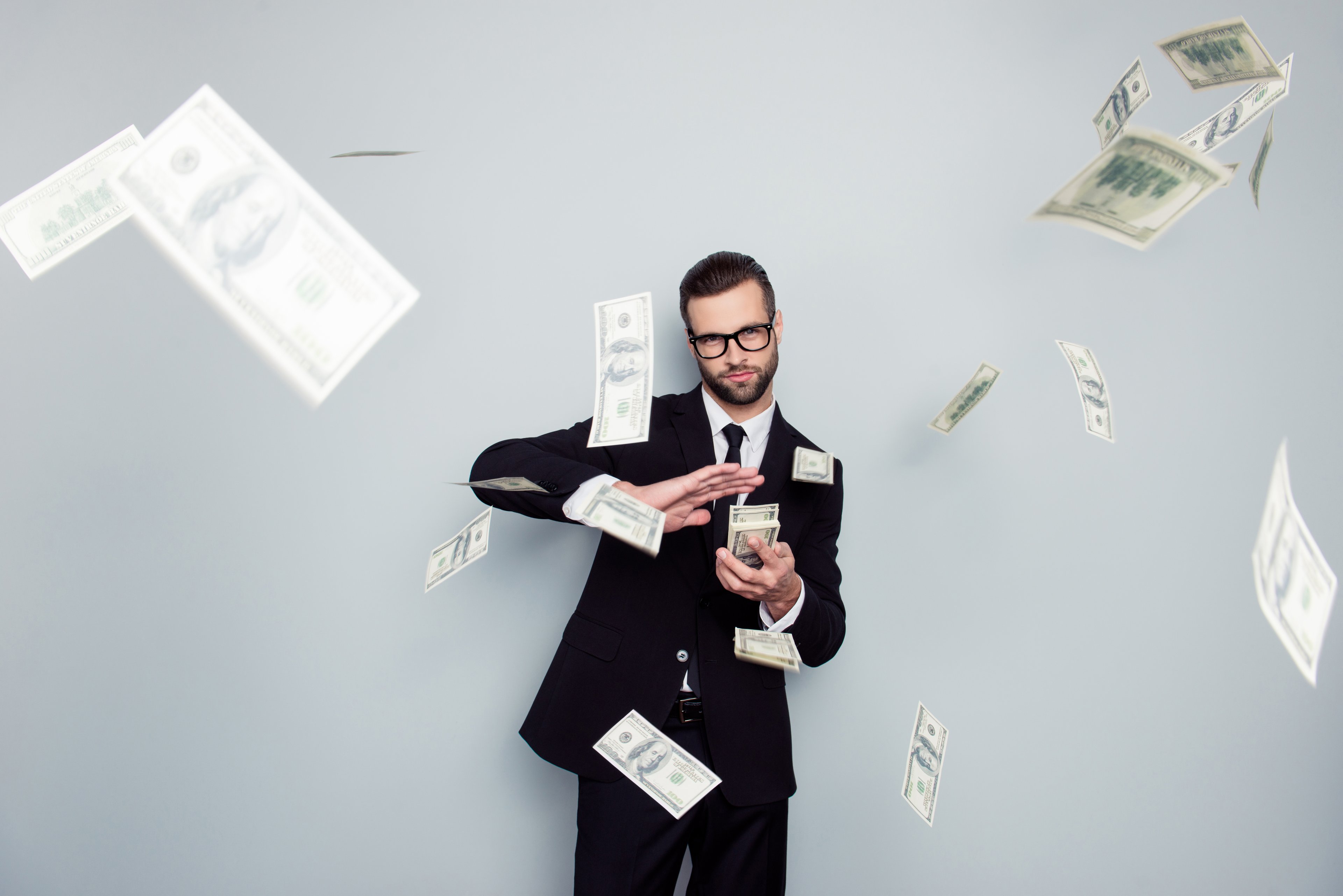 A person in a suit throwing cash bills.