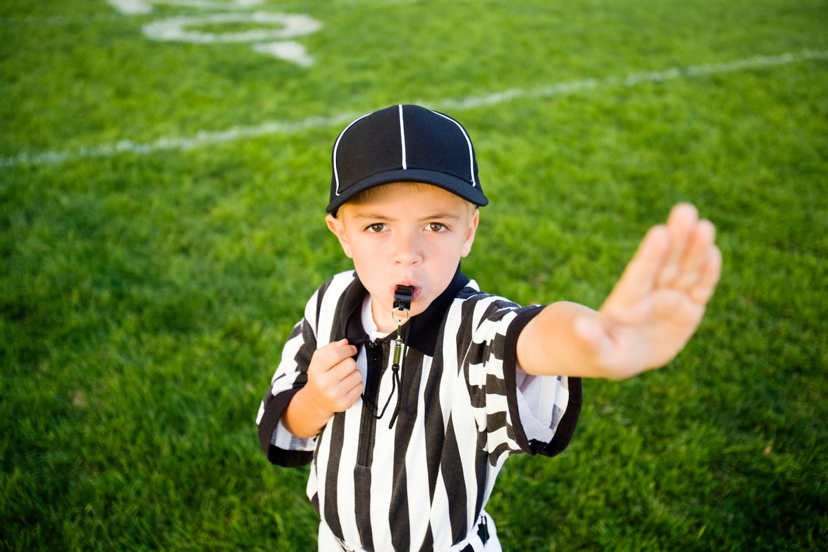 A child in a referee uniform putting their hand up to say stop.