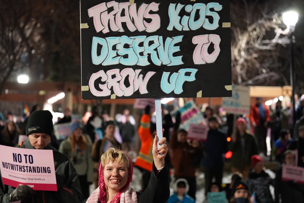 A person holds a sign at a rally that says 'Trans kids deserve to grow up'.