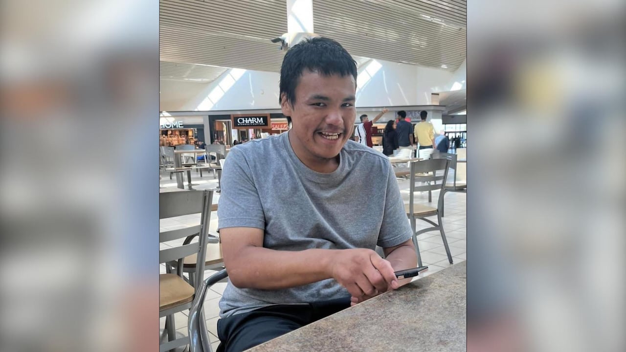 A person is seen sitting in a mall food court. They are smiling.